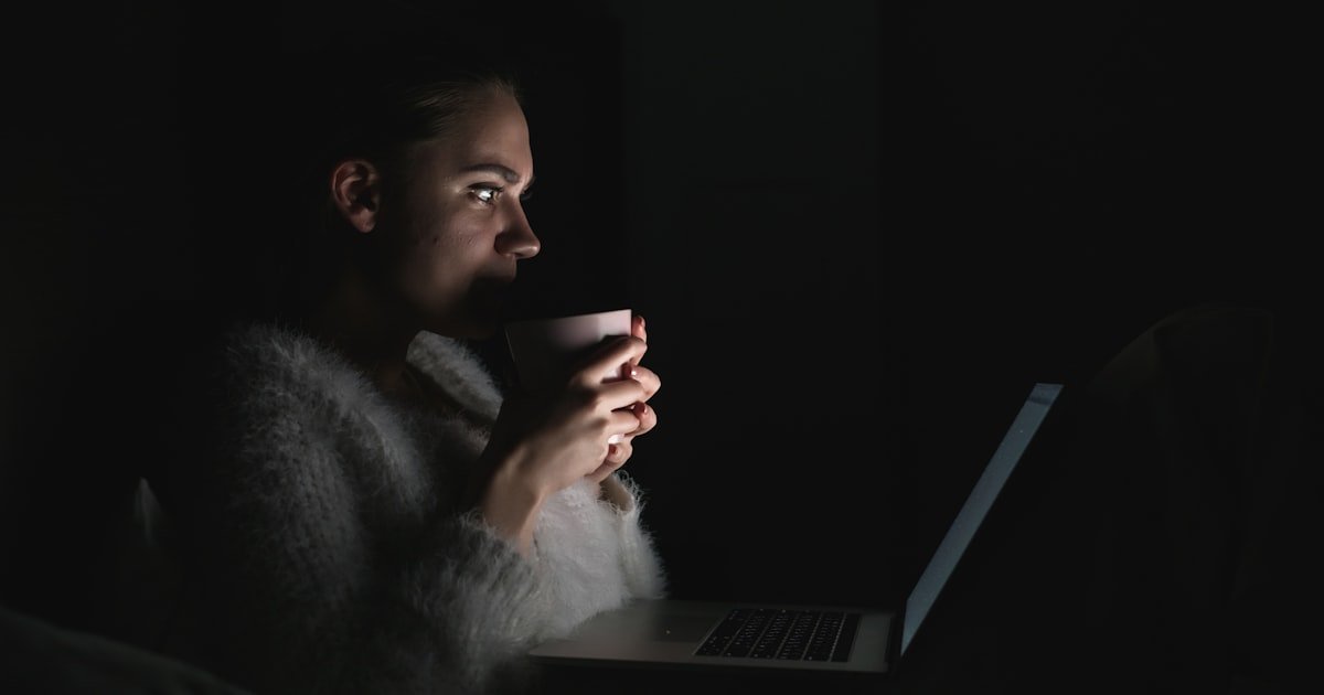 A person using a laptop at night in a dimly lit room, illustrating reduced eye strain with dark mode enabled.